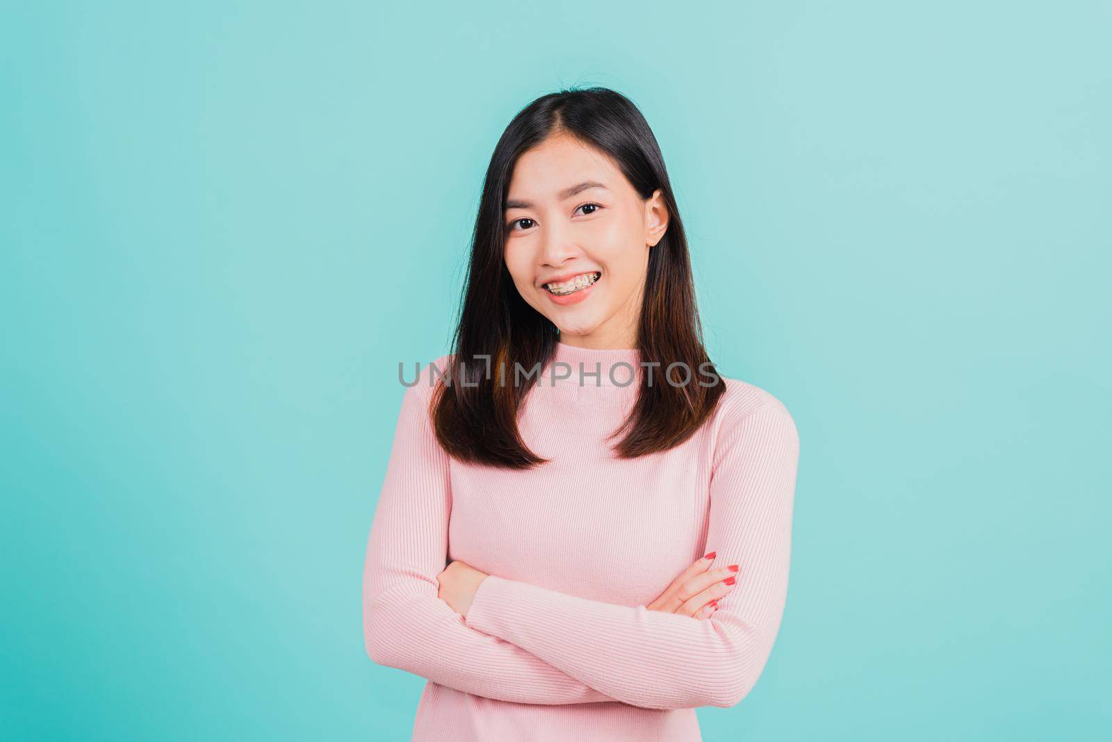 Young Asian beautiful woman smiling wear silicone orthodontic retainers on teeth with crossed arms, studio isolated on blue background, retaining tools after removable braces. Dental hygiene concept