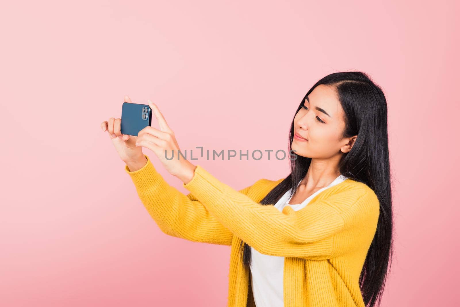 Happy Asian portrait beautiful cute young woman smiling excited  making selfie photo, video call on smartphone studio shot isolated on pink background with copy space