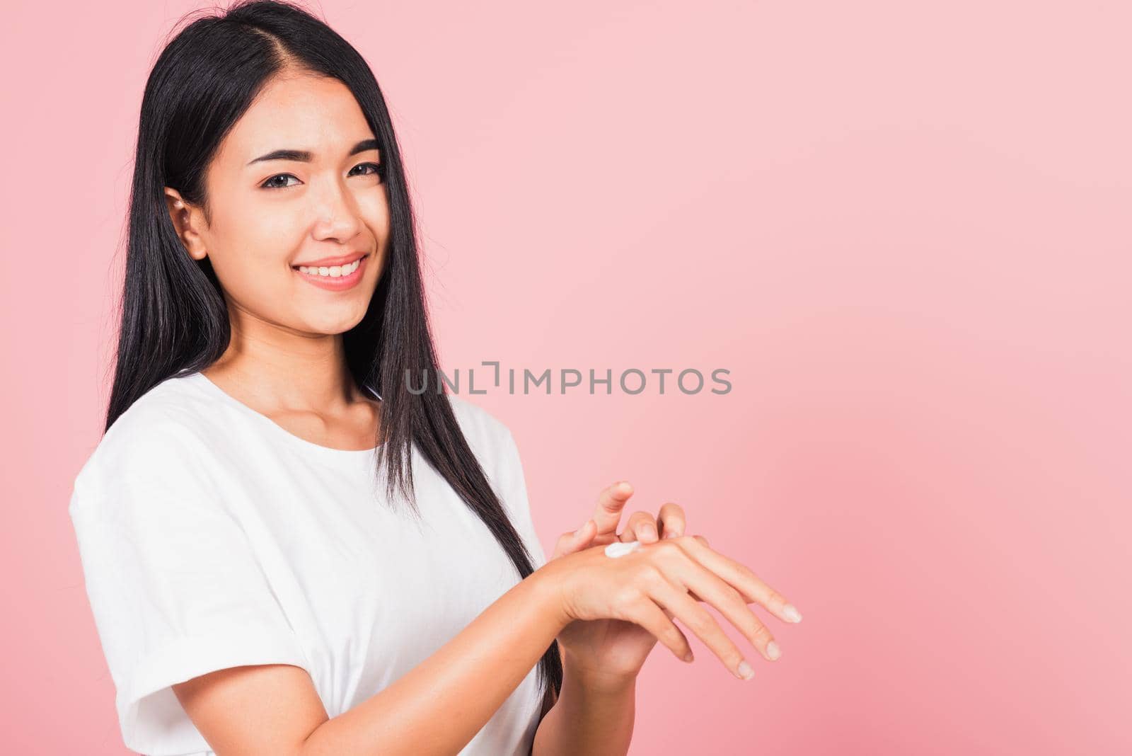 Portrait of Asian beautiful young woman applying lotion cosmetic moisturizer cream on her behind the palm skin back hand, studio shot isolated on pink background,  Hygiene skin body care concept