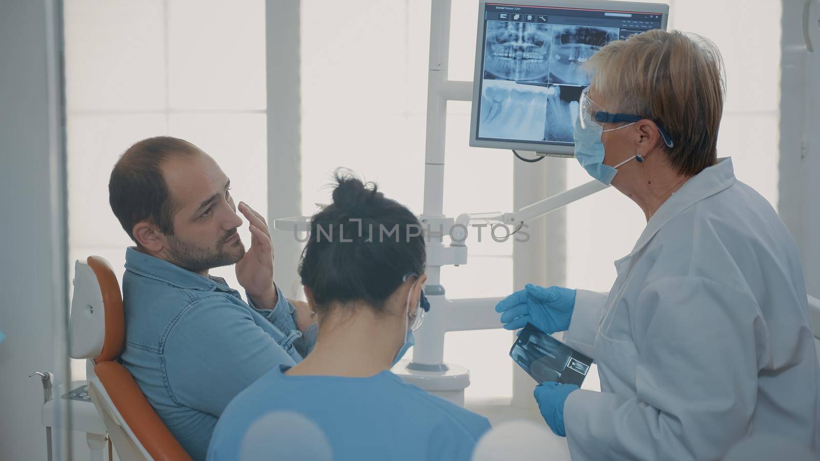 Dentist and nurse explaining x ray scan to patient with toothache in stomatology cabinet. Team of specialists doing oral care consultation to treat man in pain with denture problem.