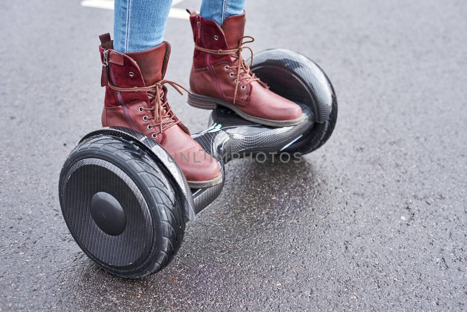 Woman using hoverboard on asphalt road, close up. Feet on electrical scooter outdoor