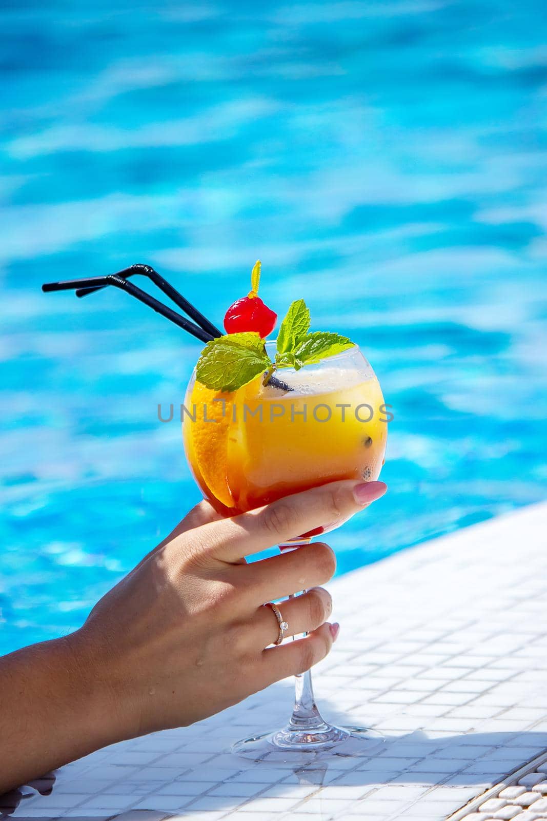 young woman is resting in the pool. Drinks a cocktail with a freshly squeezed orange. Recreation