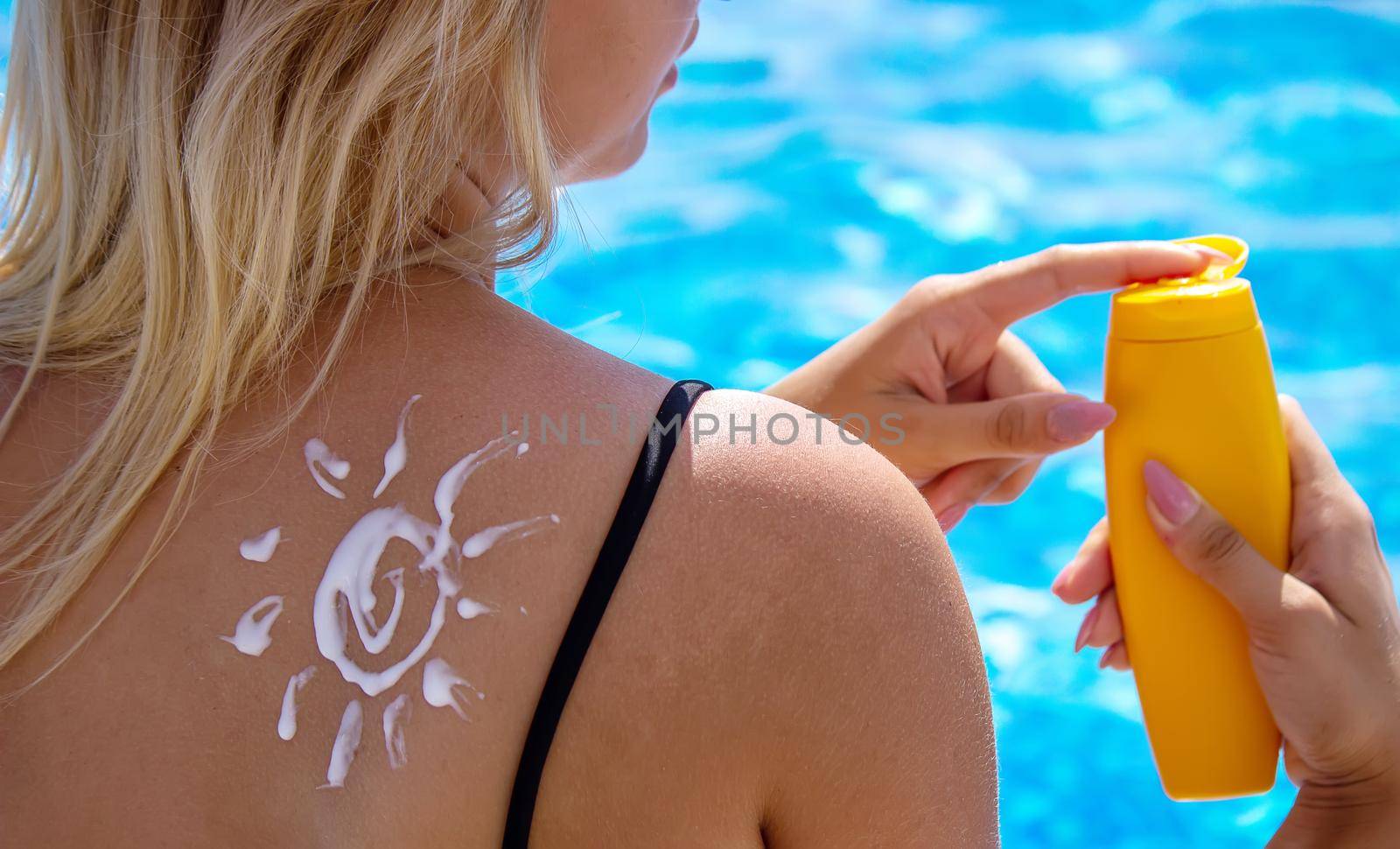 Girl with a drawing of the sun on her back with sun cream. Relaxation by the pool. Selective focus