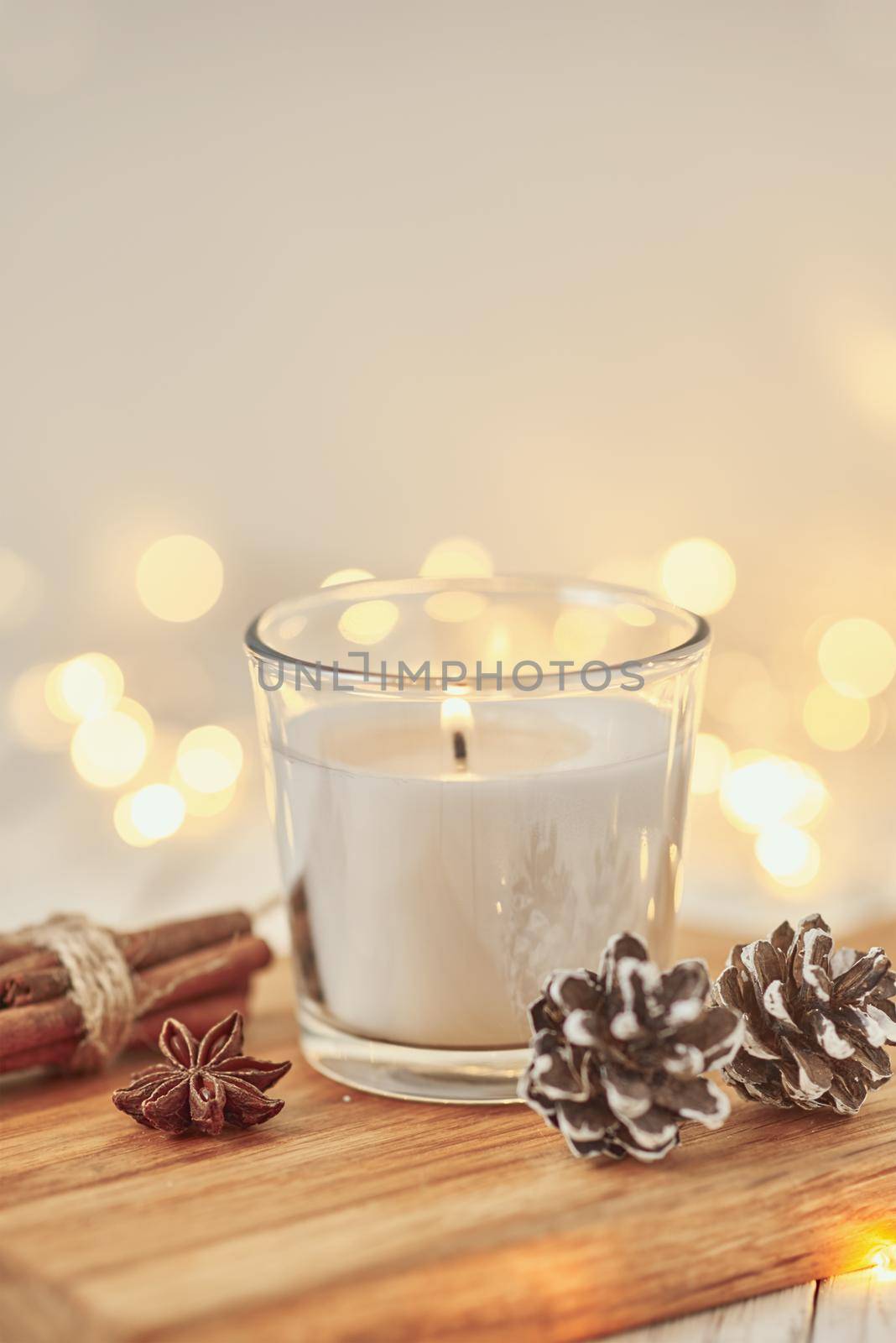 White burning candle with decorations and garland lights in bokeh on a wooden table. Cozy home and hygge concept by Lazy_Bear