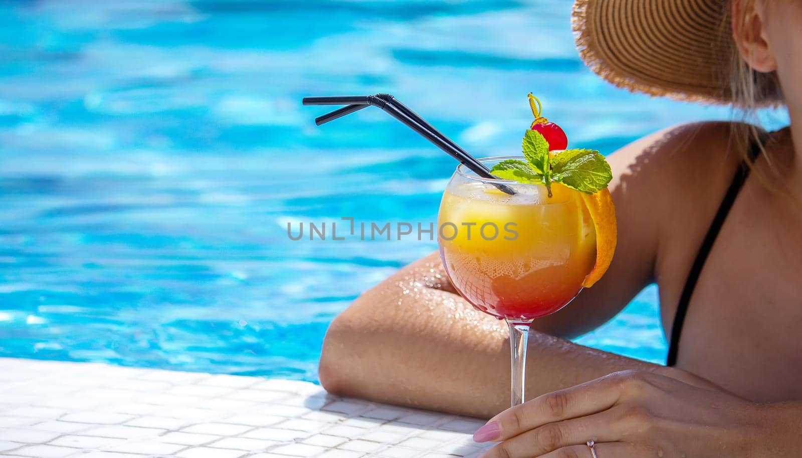 young woman is resting in the pool. Drinks a cocktail with a freshly squeezed orange. Recreation