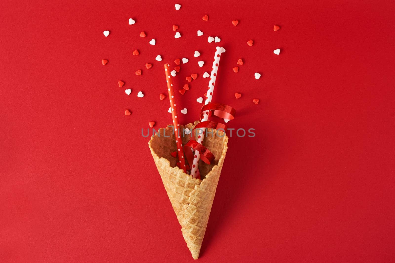 Festive ice cream cone with decorations and confetti on red backgrond, top view flat lay. Creative minimalism concept