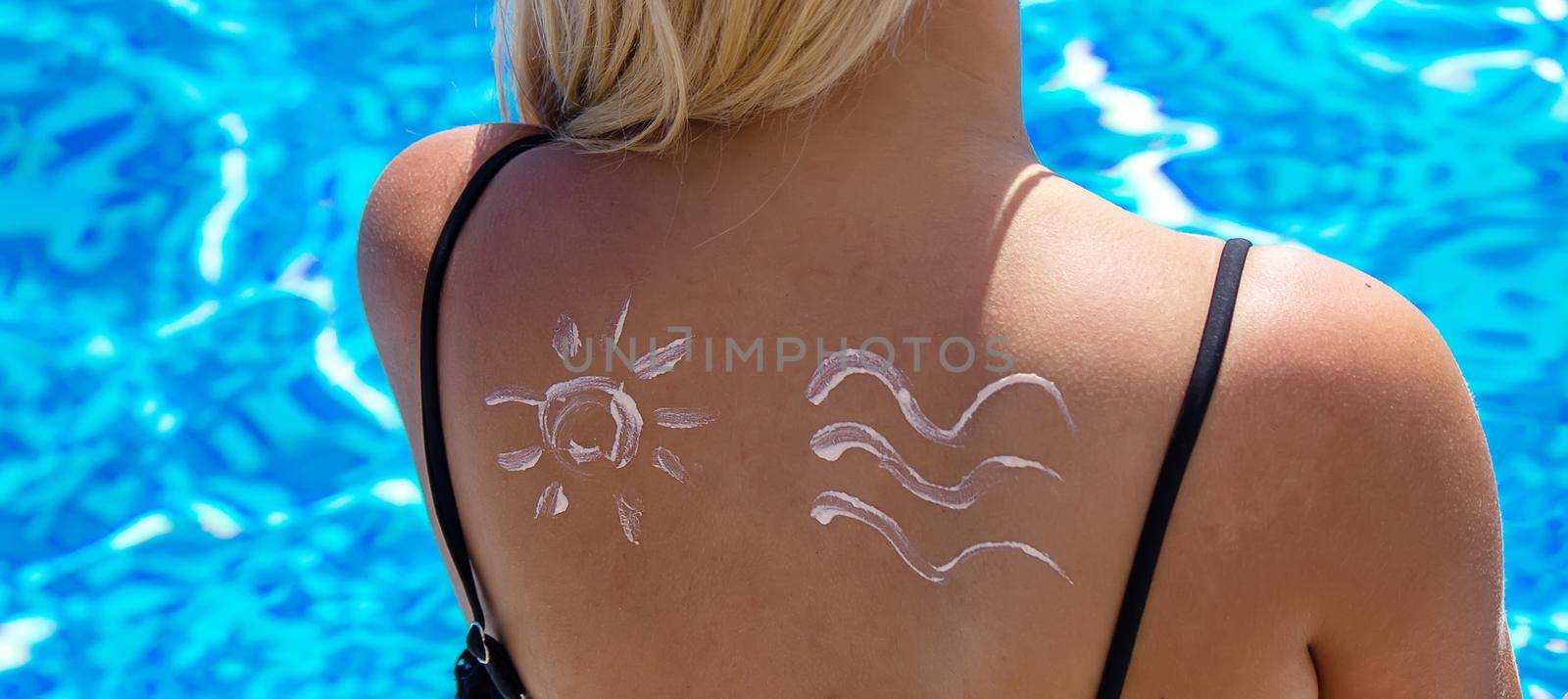 Girl with a drawing of the sun on her back with sun cream. Relaxation by the pool. Selective focus