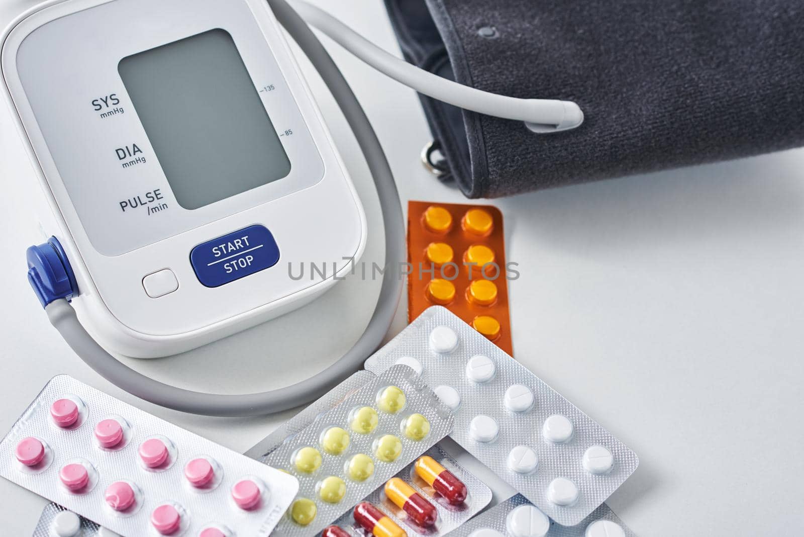 Digital blood pressure monitor and medical pills on white table. Healthcare and medicine concept