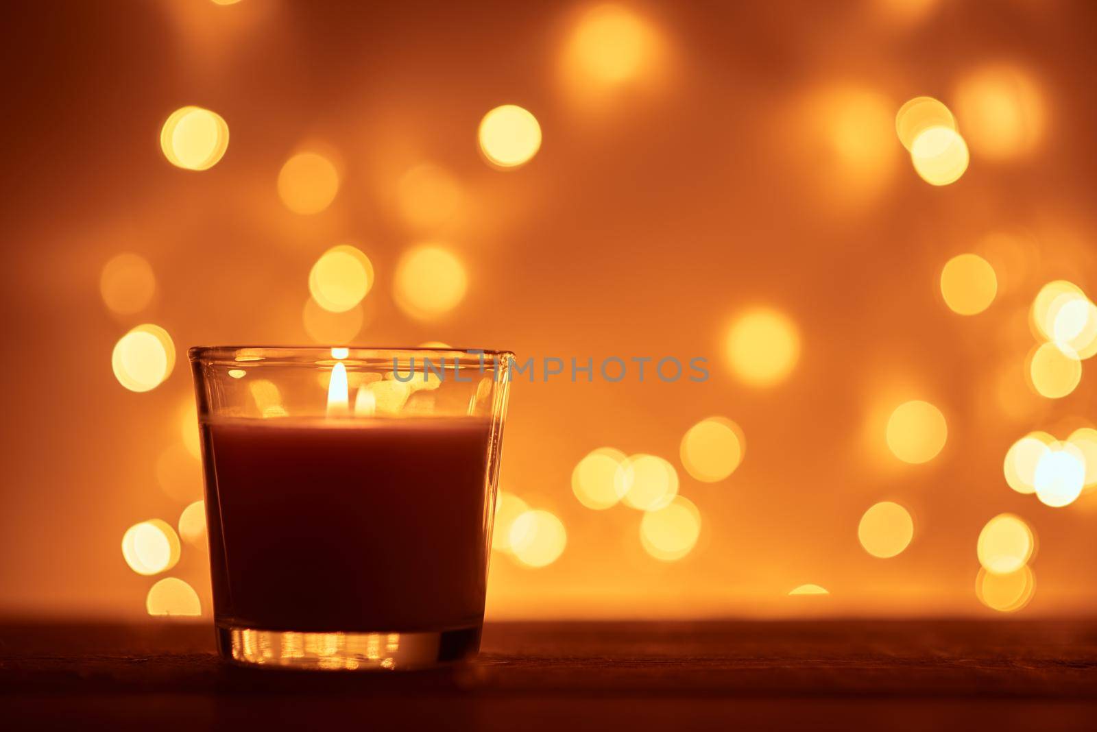 Silhouette of burning candle with golden blurred lights on dark background