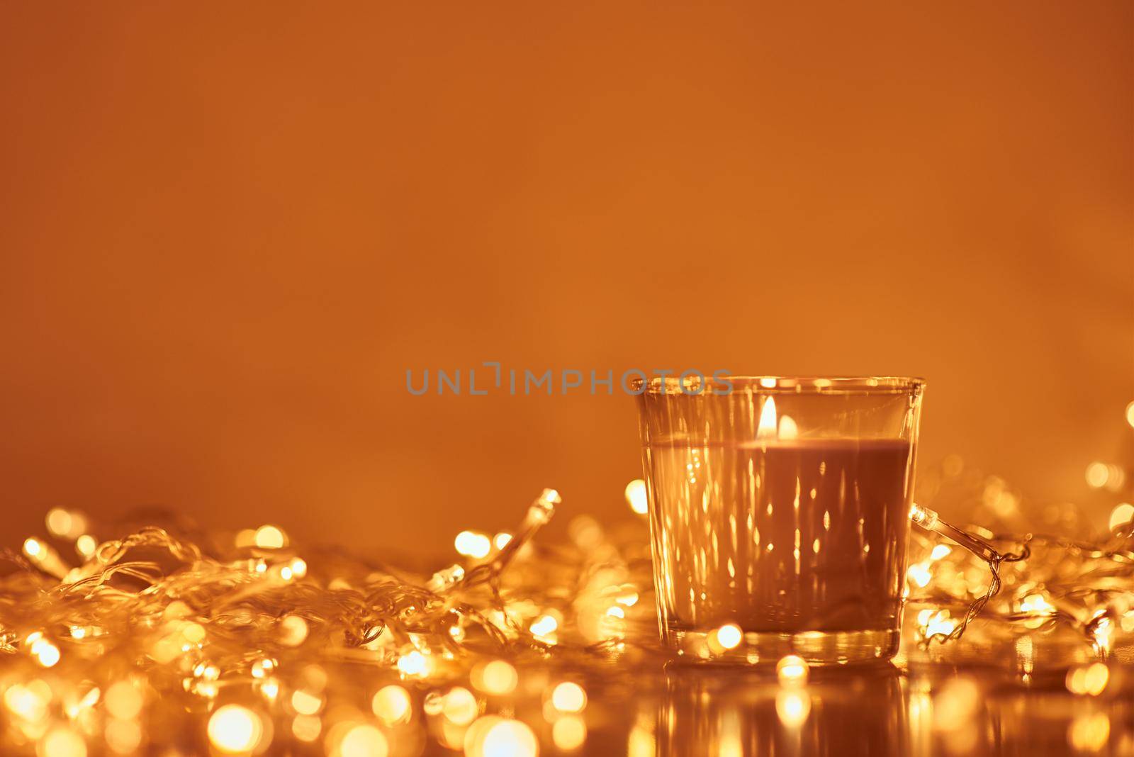 Burning candle with golden garland lights in bokeh on dark background