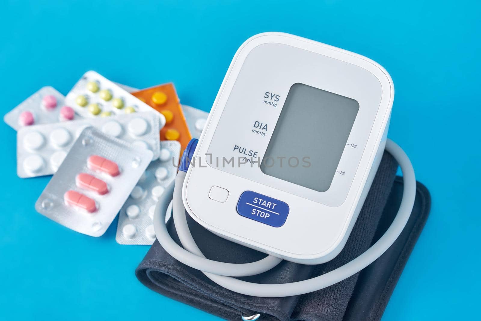 Digital blood pressure monitor and medical pills on blue background. Healthcare and medicine concept