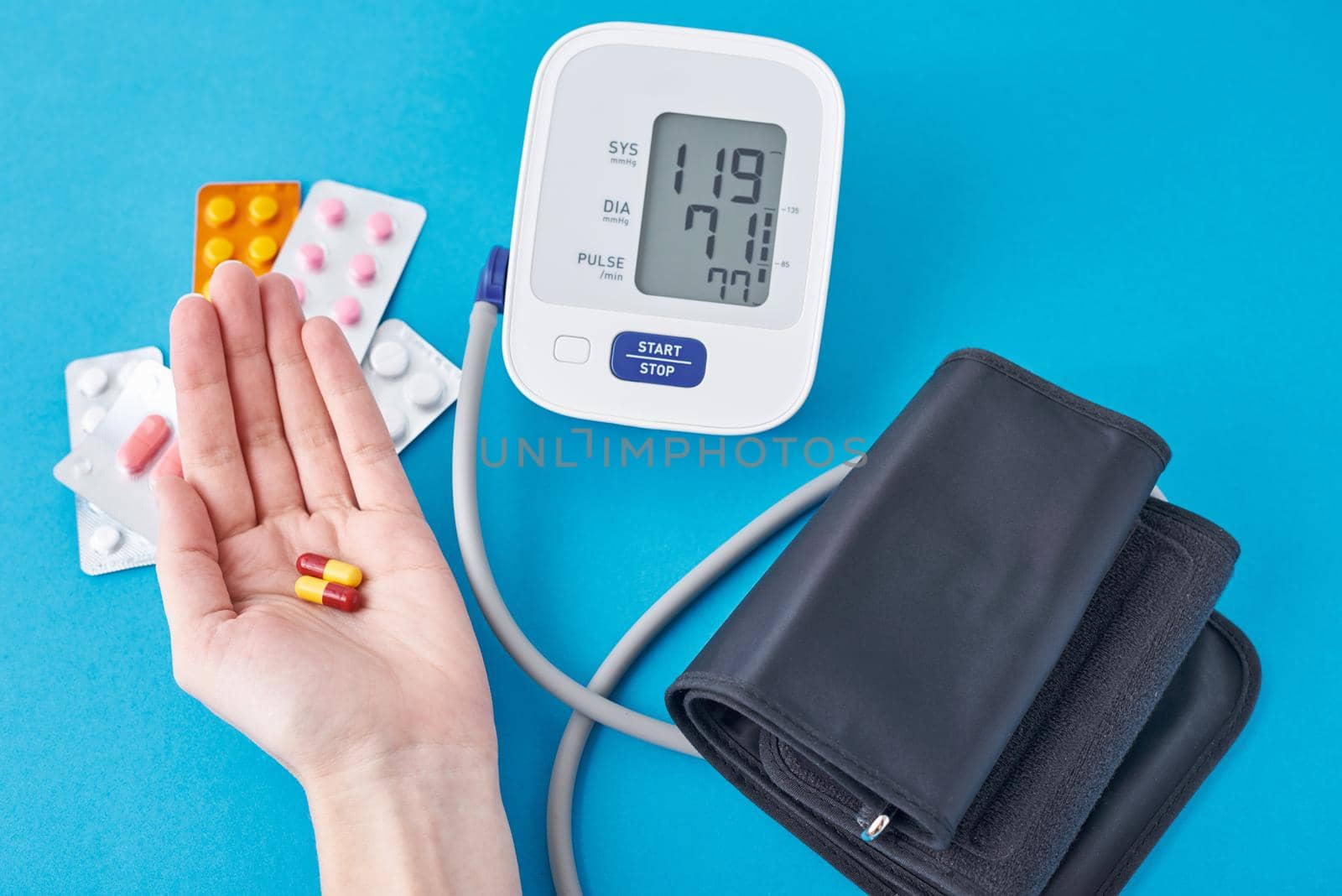 Digital blood pressure monitor and medical pills in hand on a blue background. Healthcare and medicine concept by Lazy_Bear