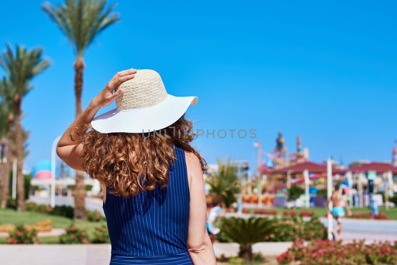 Woman in hat and blue dress go for a walk in hotel resort