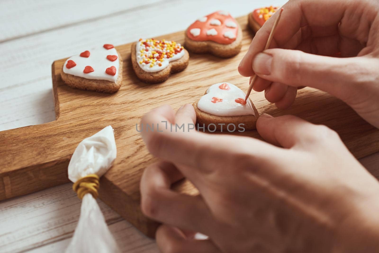 Decorating gingerbread cookies with icing. Woman hands decorate cookies in shape of heart, closeup