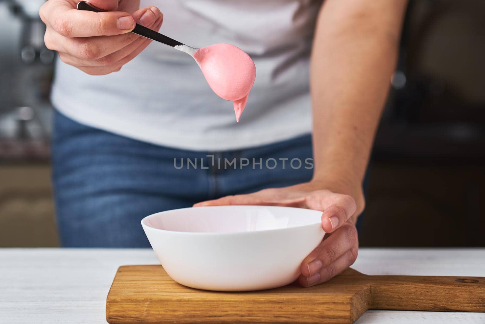 Woman whisking red cream for decorating cookies in bowl on kitchen, closeup