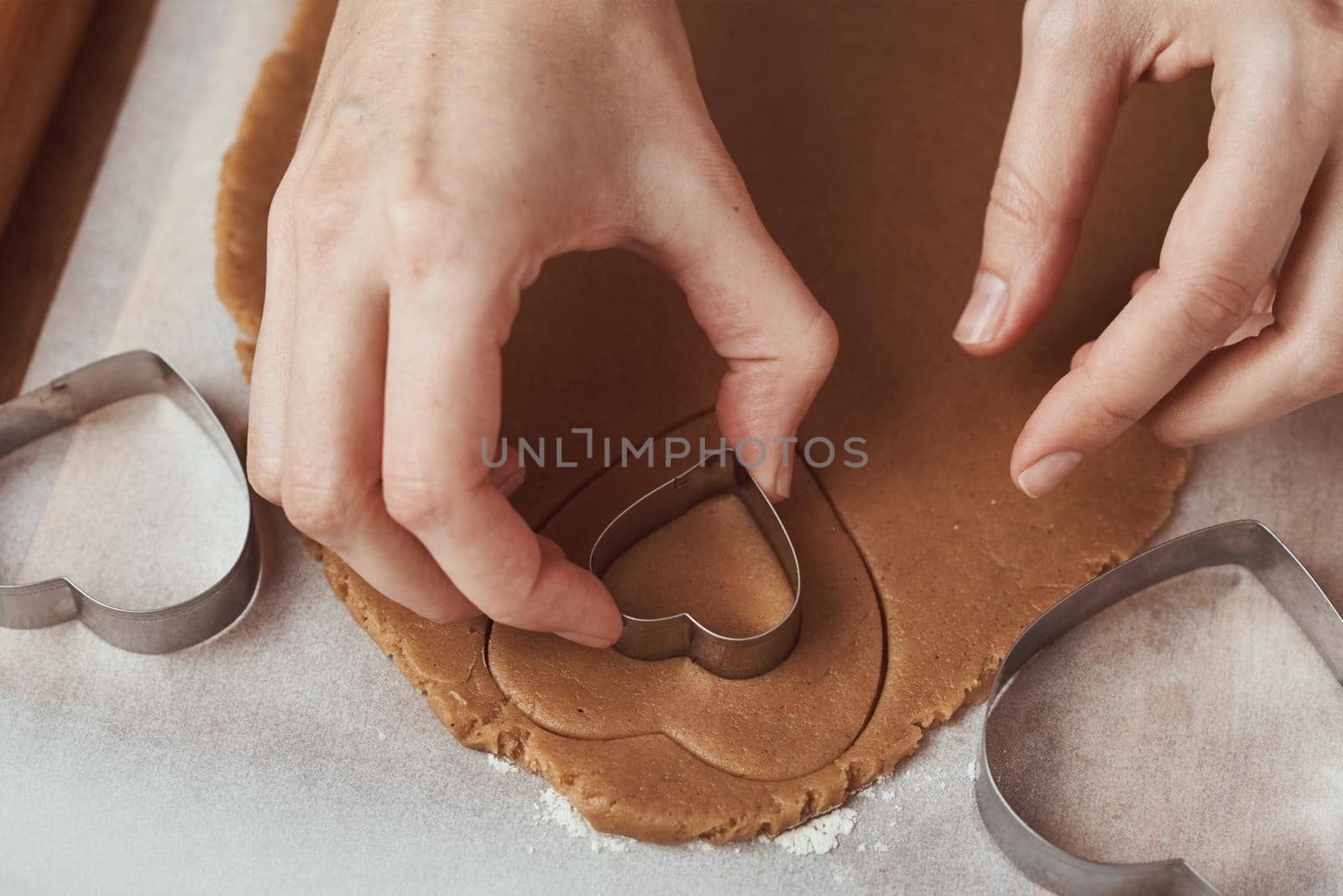 Making gingerbread cookies in the shape of a heart for Valentines Day. Woman hand use cookie cutter. Holiday food concept by Lazy_Bear