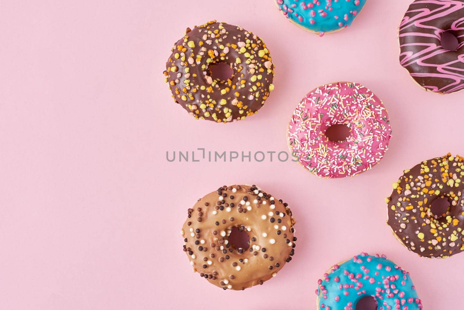 Pattern with different types of colorful donats decorated sprinkles and icing on pastel pink background, top view flat lay