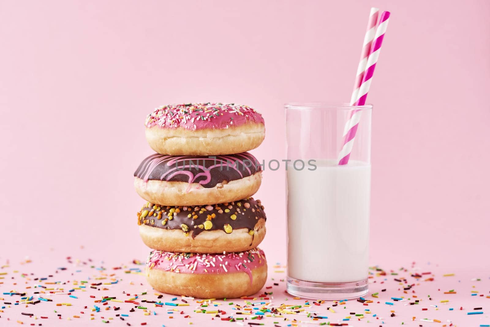 Stack of colorful donuts decorated and glass of milk on pink background
