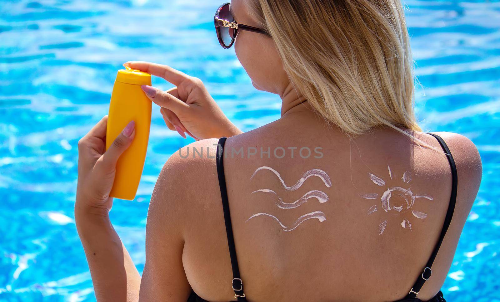 Girl with a drawing of the sun on her back with sun cream. Relaxation by the pool. Selective focus