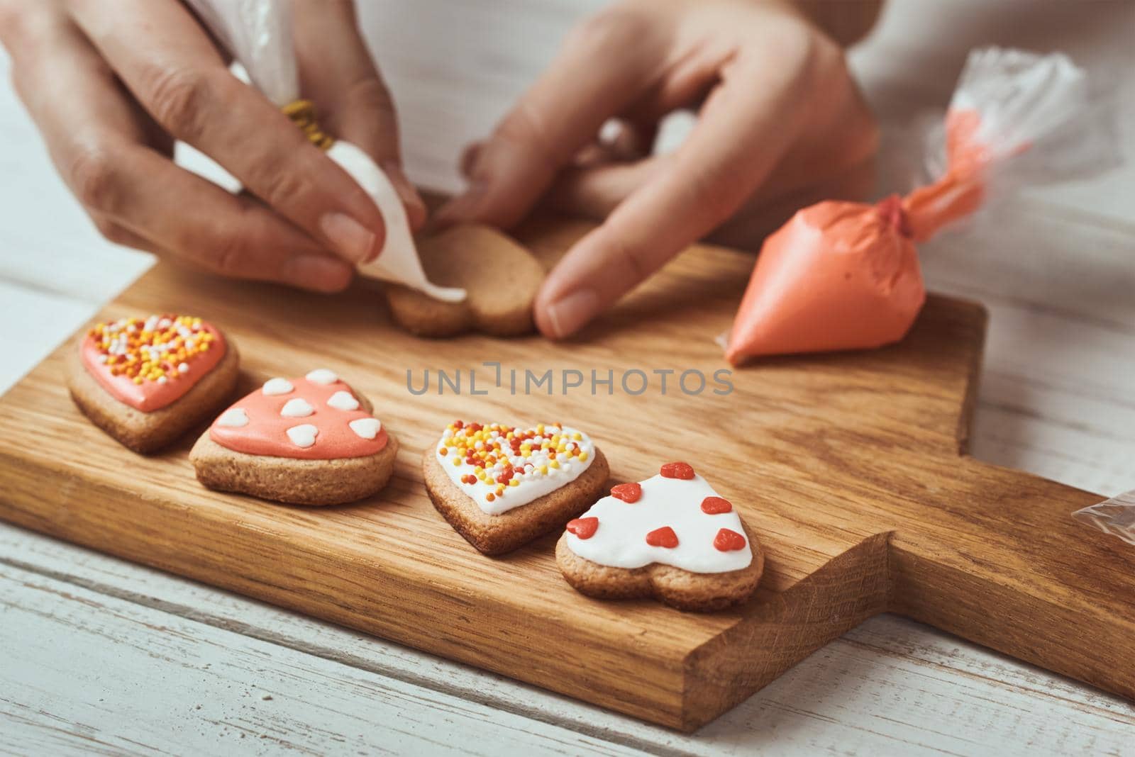 Decorating gingerbread cookies with icing. Woman hand decorate cookies in shape of heart, closeup by Lazy_Bear