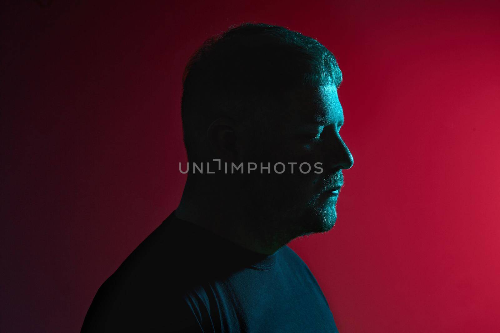 Epitome of masculinity. Portrait of a good-looking, bearded young guy in a black sweater posing against a colorful background. Modern and dramatic profile foto in twilight.