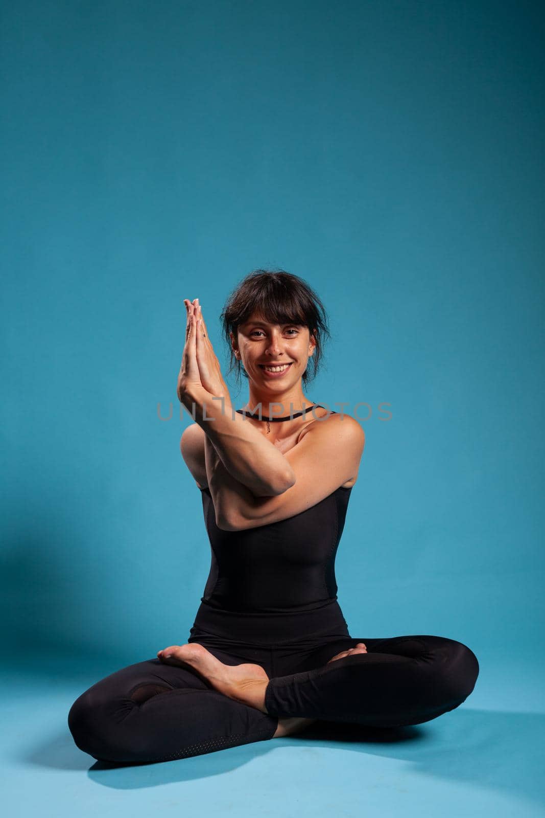 Portrait of smiling zen woman trainer standing in lotus position holding arms in crossed position practicing spiritual meditation. Athletic person working at healthy lifestyle stretching body muscles