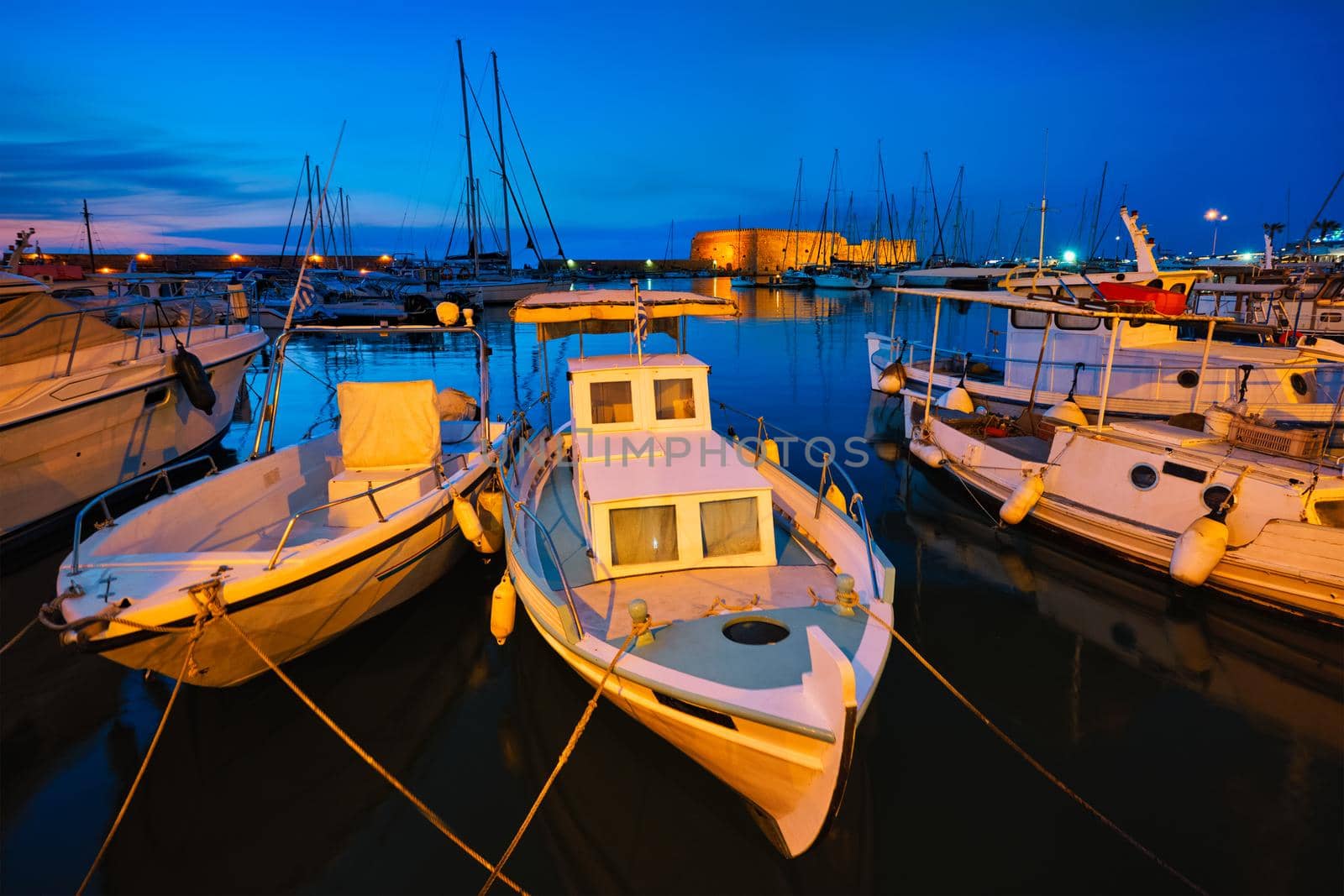 Venetian Fort castle in Heraklion and moored Greek fishing boats in port, Crete Island, Greece in twilight