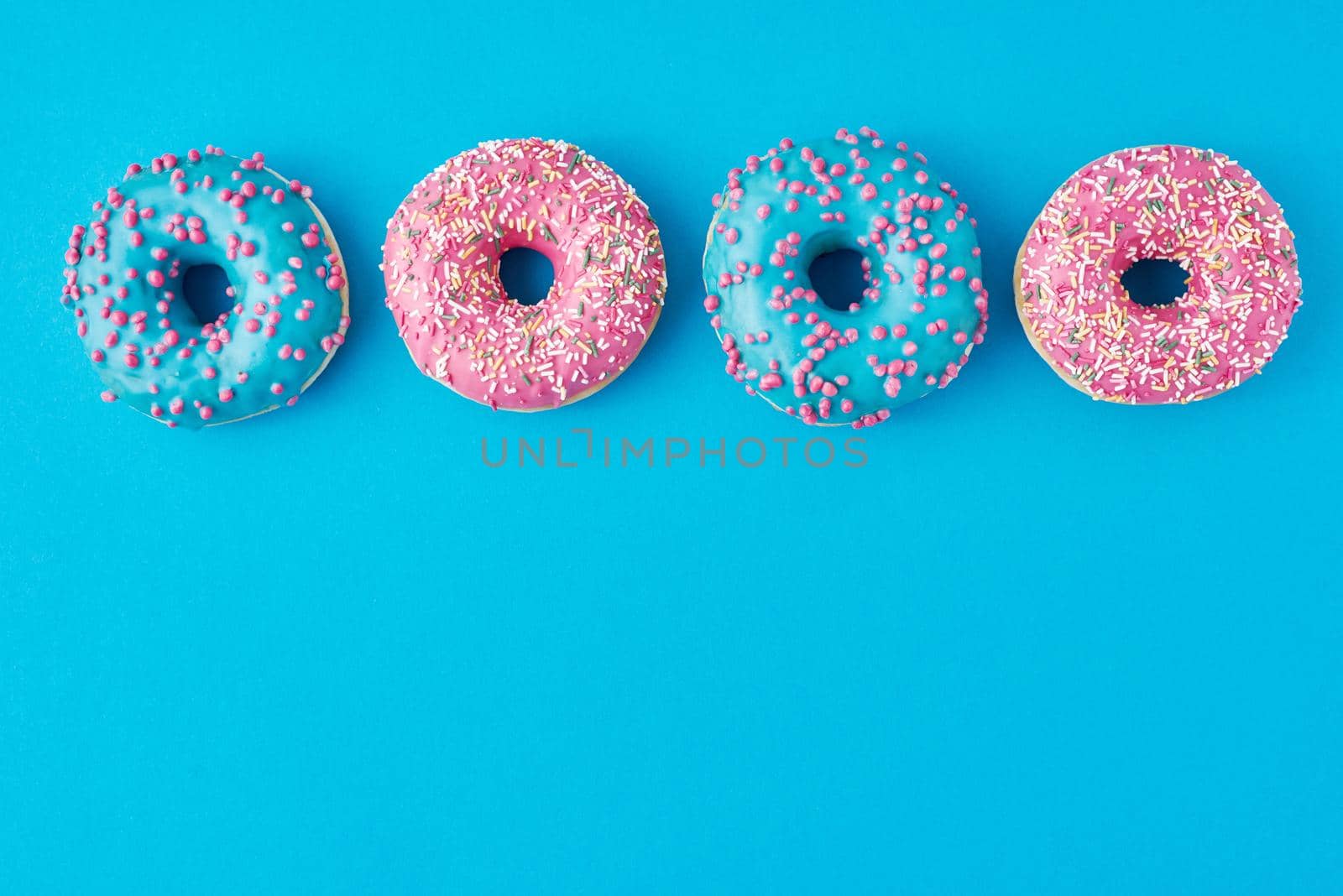 Different types of colorful donats decorated sprinkles and icing on blue background