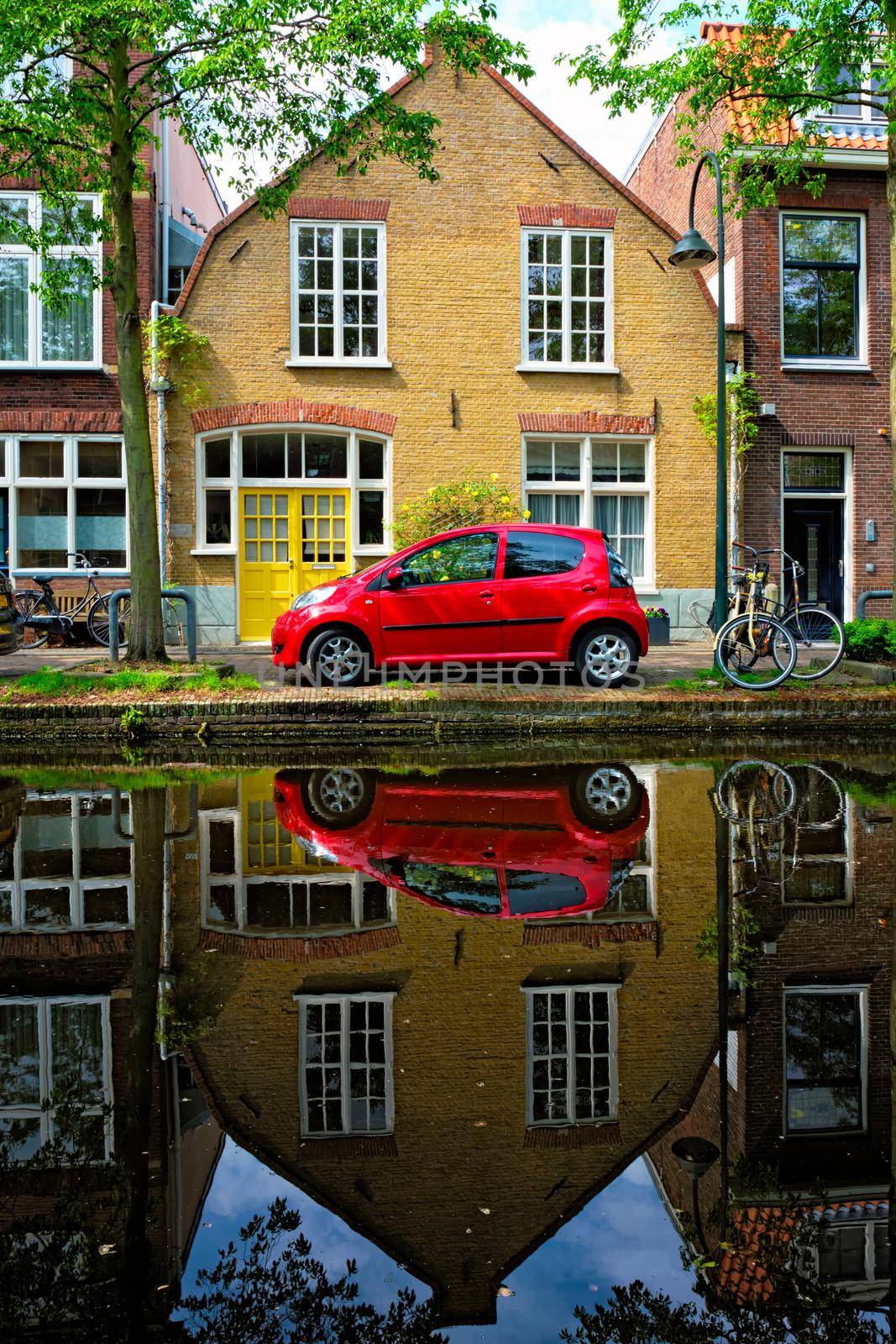 Red car on canal embankment in street of Delft with reflection and bicycle. Delft, Netherlands