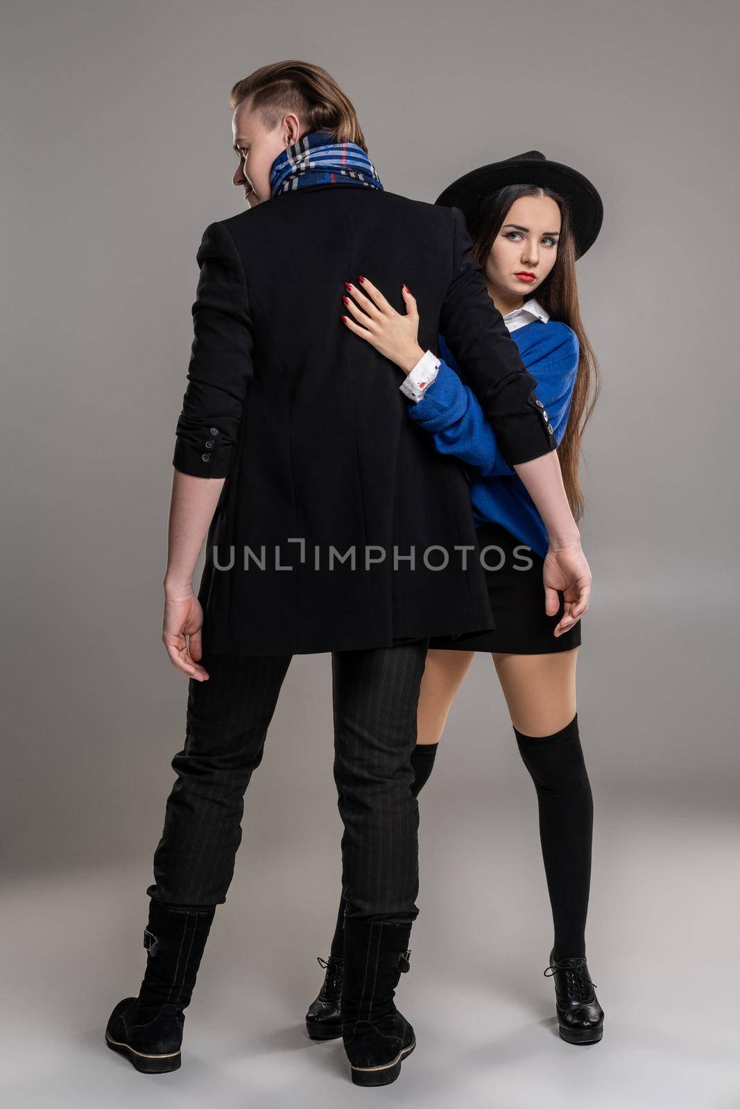Young loving couple. Studio shot of a pretty young maiden and handsome man. They are in black outlet clothes and stylish hat posing over a gray studio background. Fashion shot. Sincere emotions concept. Copy space.