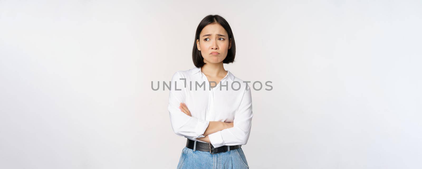 Image of sad office girl, asian woman sulking and frowning disappointed, standing upset and distressed against white background.