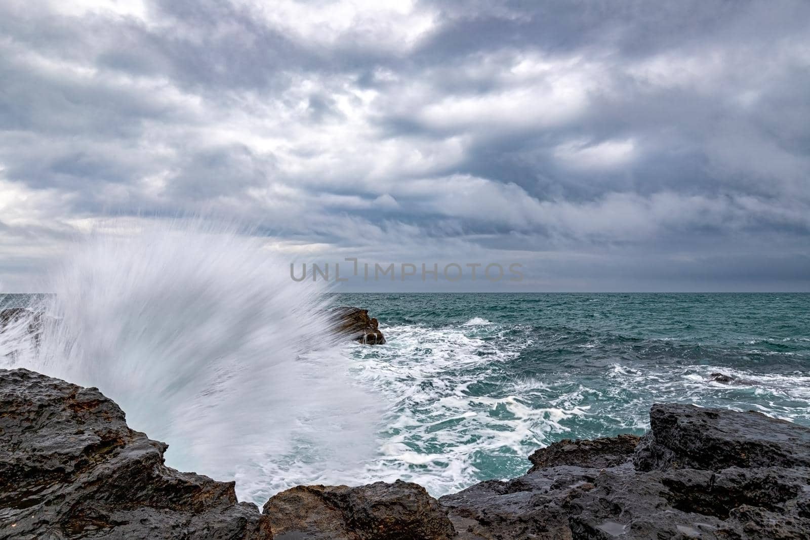 Stunning wave splash at rocky shore and scenic clouds