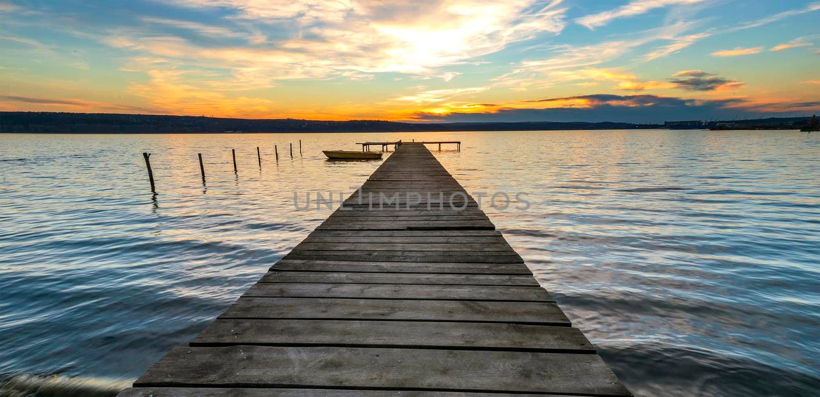 Exciting twilight at the shore with wooden pier and moored boat by EdVal