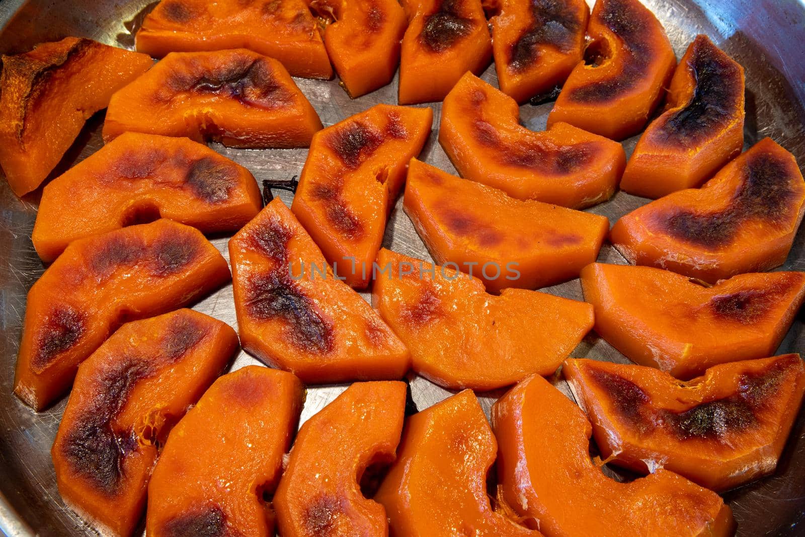 Freshly roasted pumpkin in small slices in a pan. View from above