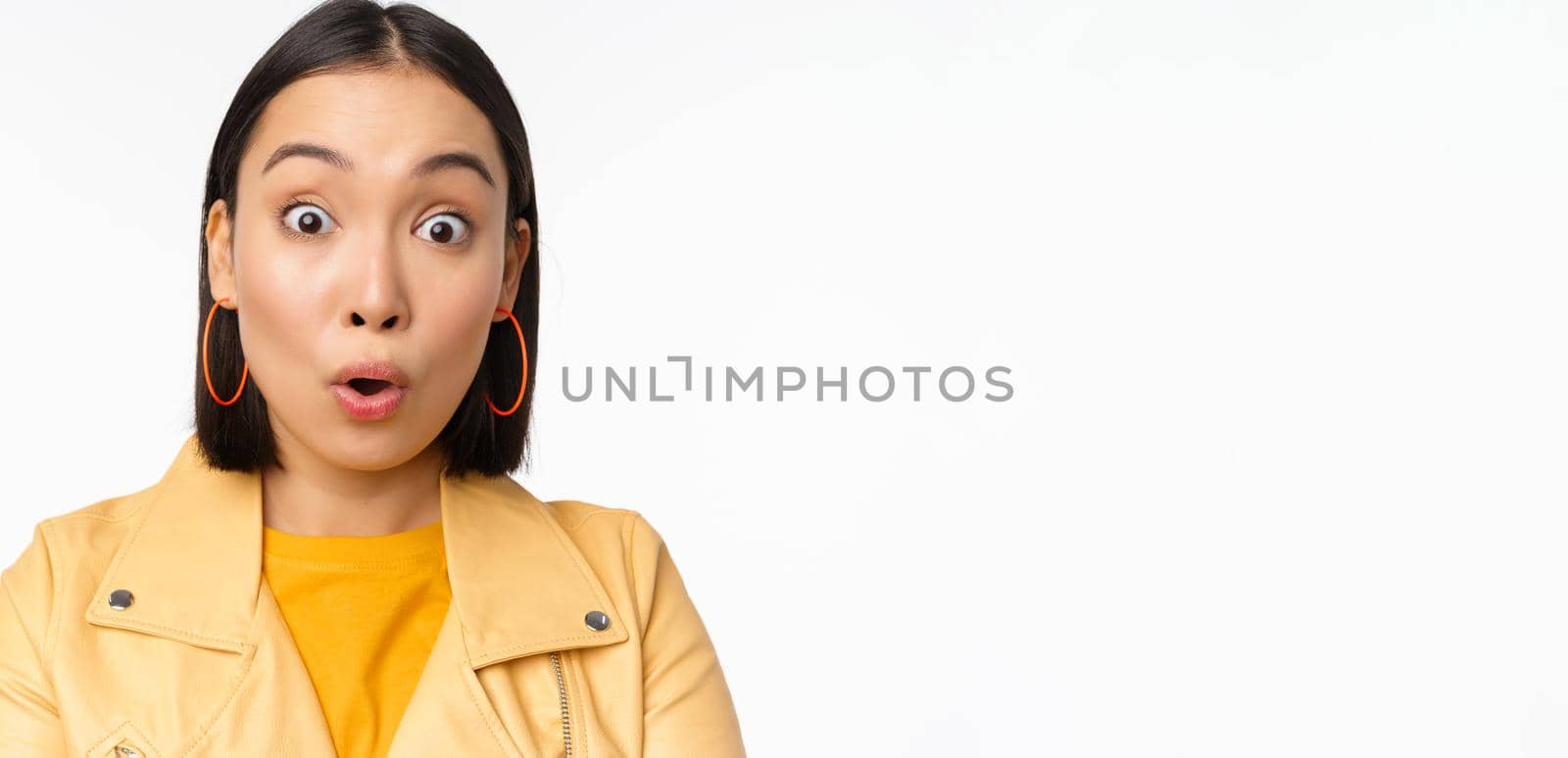 Close up of impressed asian girl, say wow, looking amazed at camera, standing in casual clothes over white background. Copy space