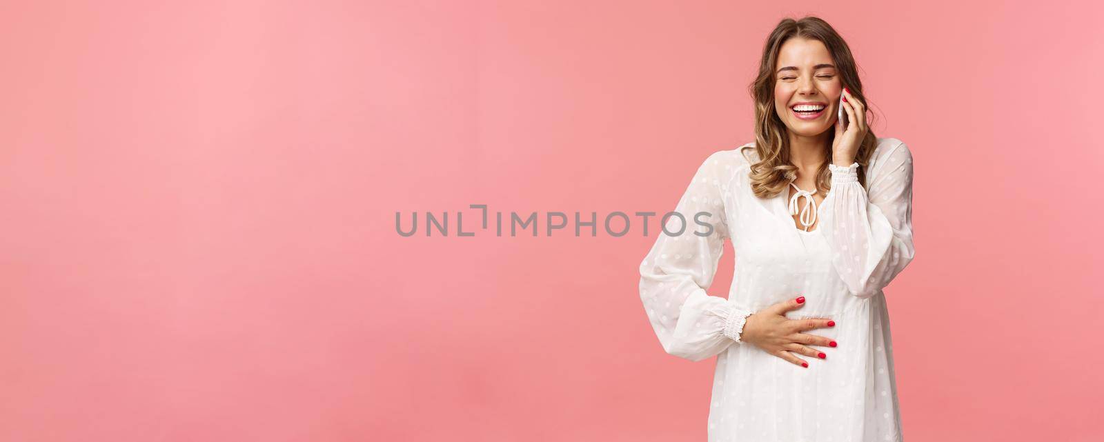 Portrait of joyful happy bright young girl in white dress, having fun, speaking to friend, calling person mobile phone, laughing and touching belly, close eyes smiling, hold smartphone near ear by Benzoix