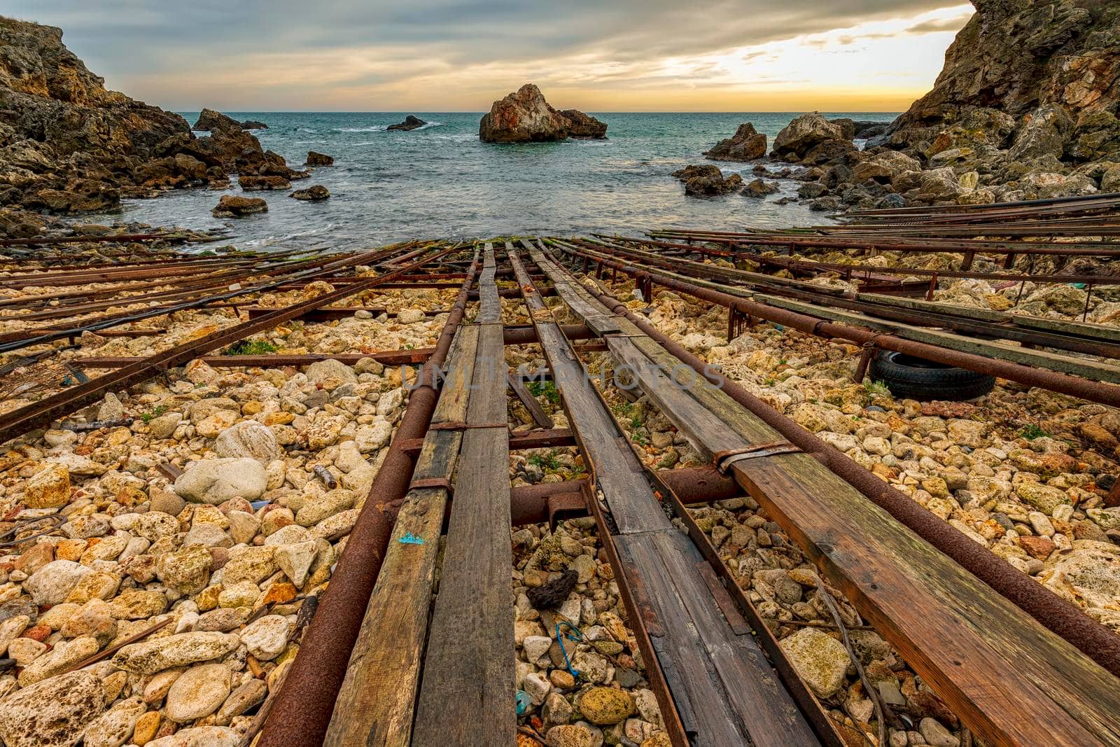 Scenic view from the shore with rails for transporting boats and big rocks by EdVal