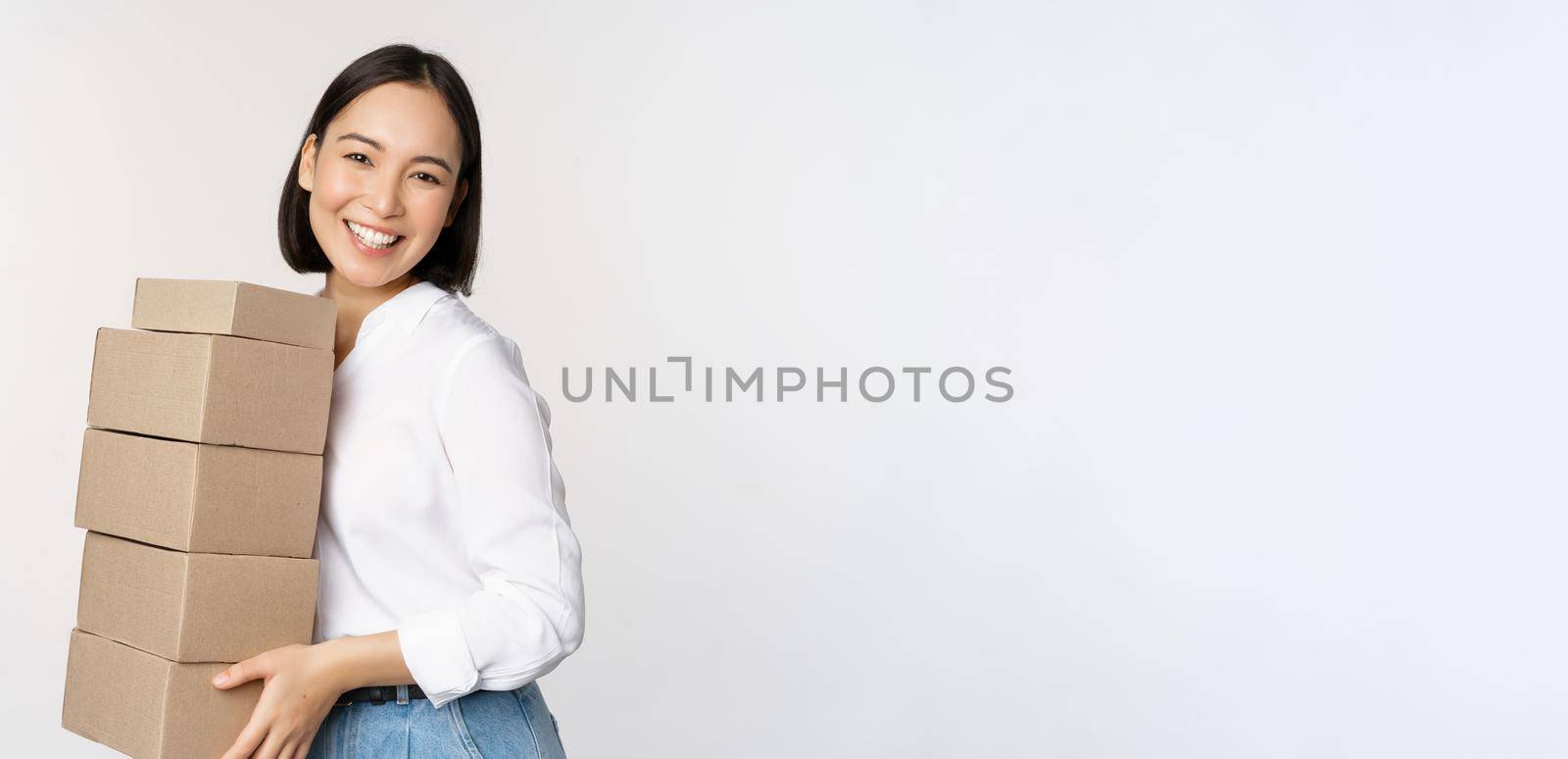 Portrait of young asian woman holding boxes, carry delivery goods. Korean female entrepreneur assemble order, standing voer white background.