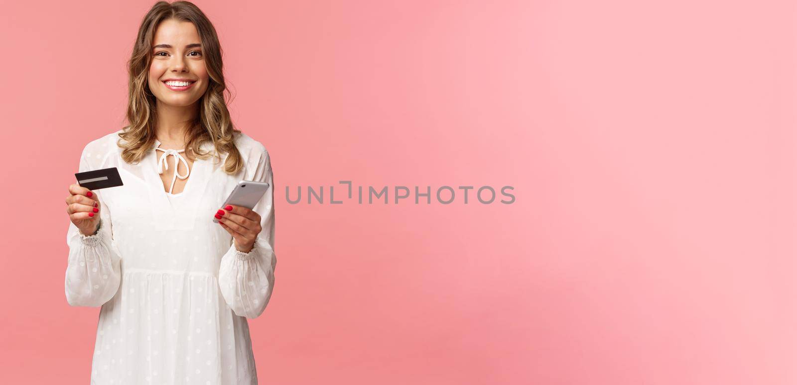 Portrait of happy smiling blond woman order food online, use application for shopping internet store, holding credit card and smartphone, grinning delighted at camera, pink background by Benzoix