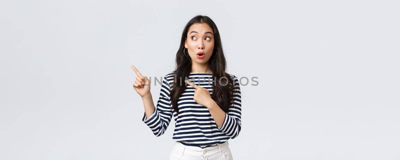 Lifestyle, people emotions and casual concept. Surprised and excited cute asian female customer telling about big sale, promo discounts, pointing fingers upper left corner and look amazed by Benzoix