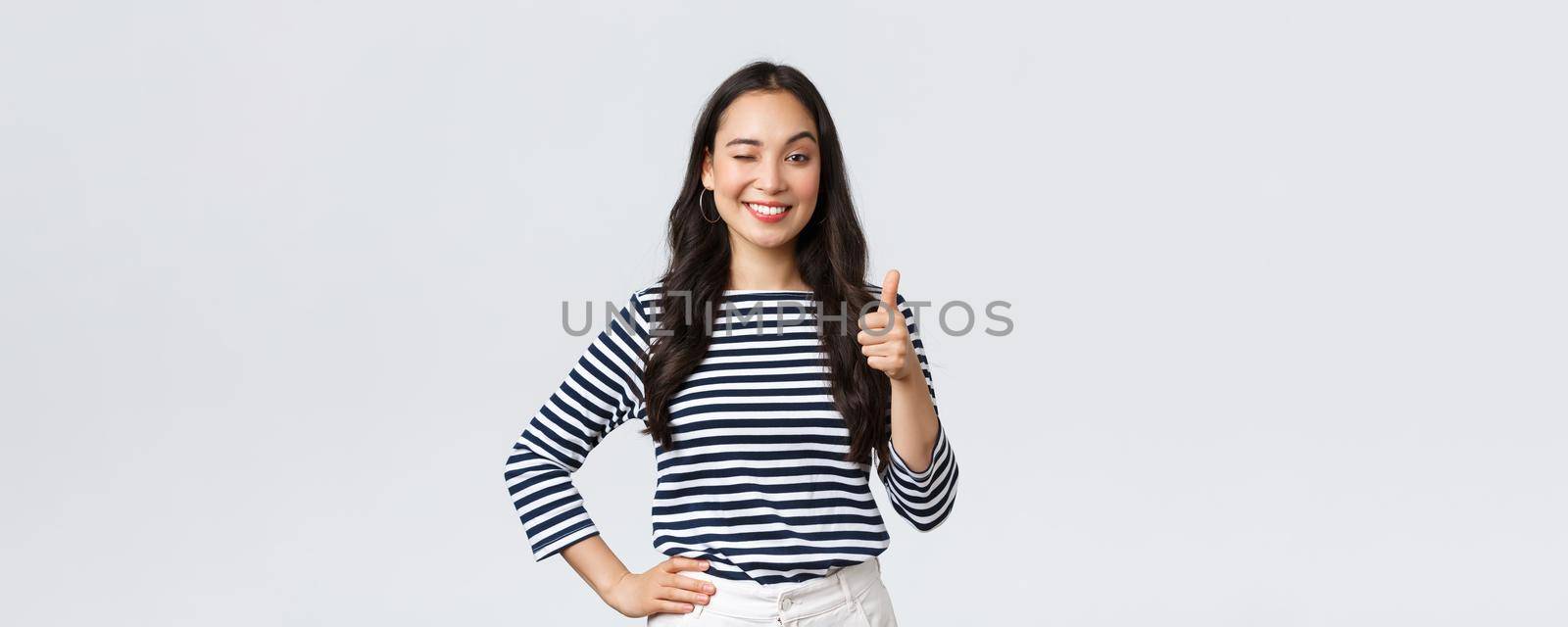 Lifestyle, beauty and fashion, people emotions concept. Cheerful cute asian girl thumb-up in approval, wink encouraging and smiling, praising nice job, say well played as congratulate with win by Benzoix