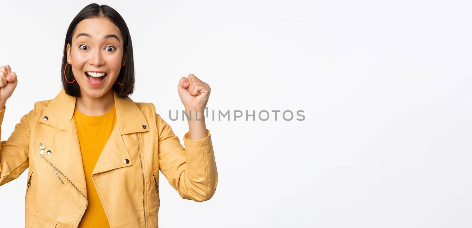 Image of asian woman dancing and smiling happy, celebrating victory, triumphing, standing over white background by Benzoix
