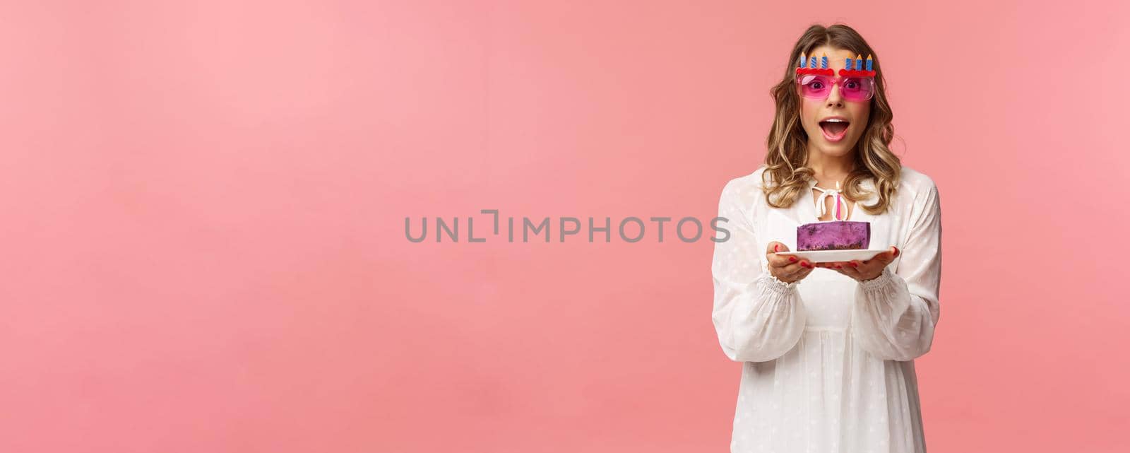 Holidays, spring and party concept. Excited, happy attractive blond woman in white dress, wearing funny b-day glasses, holding birthday cake with lit candle, making wish smiling camera by Benzoix