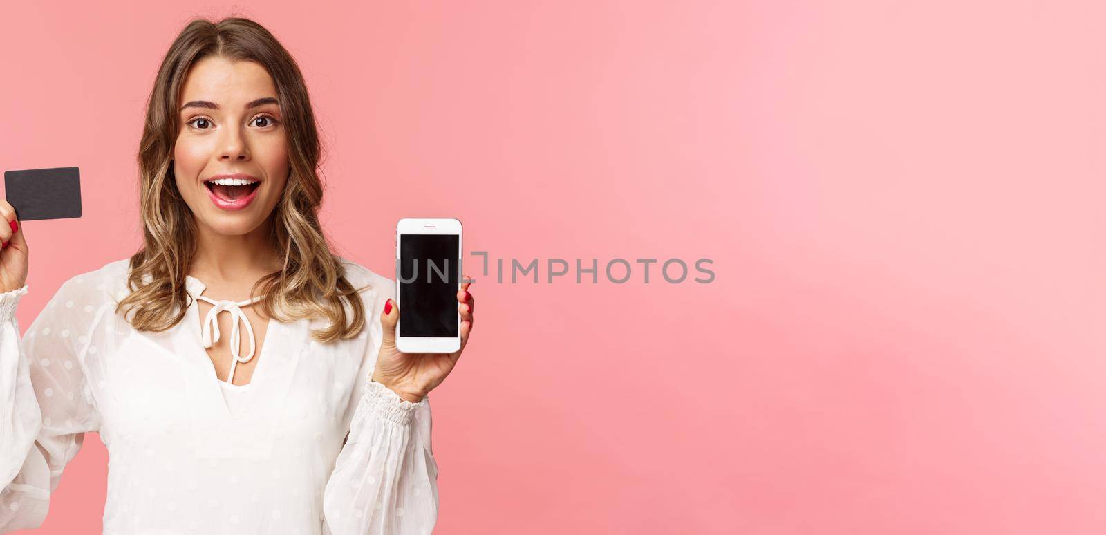 Finance, shopping and technology concept. Close-up portrait of excited blond attractive girl in white dress, showing credit card and mobile phone, advertise online store, smartphone app.