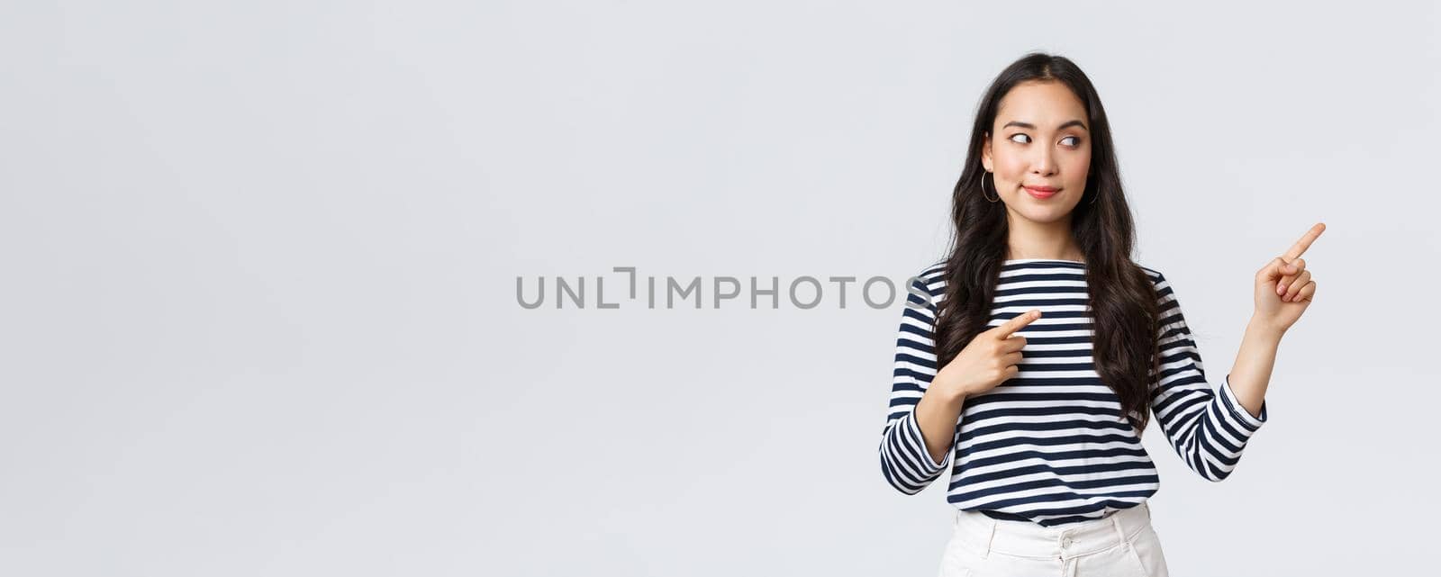 Lifestyle, beauty and fashion, people emotions concept. Intrigued stylish young asian woman looking and pointing at right banner with pleased tempting expression, wants buy something.