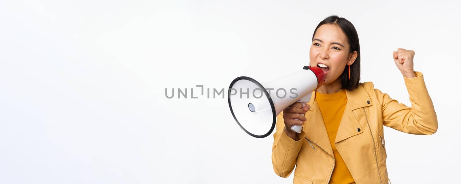 Portrait of young asian woman protester, screaming in megaphone and protesting, standing confident against white background.