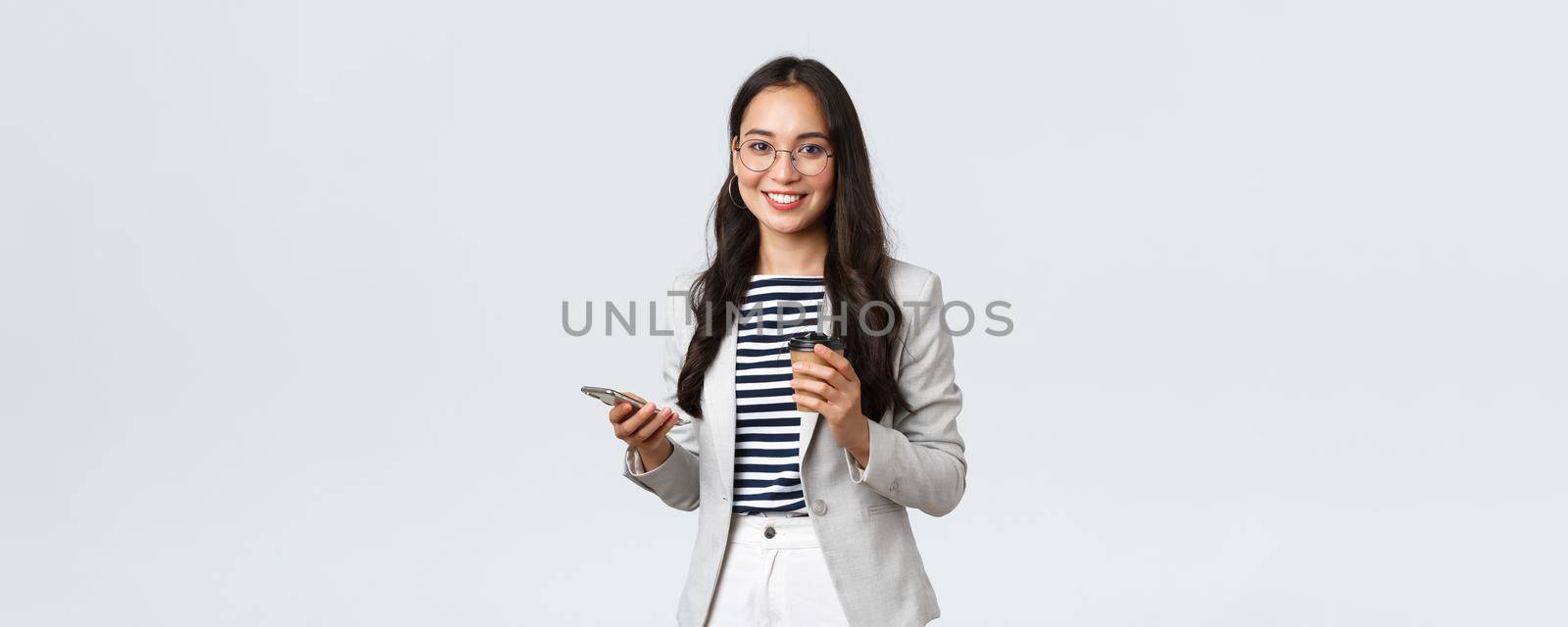 Business, finance and employment, female successful entrepreneurs concept. Professional asian businesswoman in glasses, having lunch, drinking takeaway coffee and using mobile phone by Benzoix