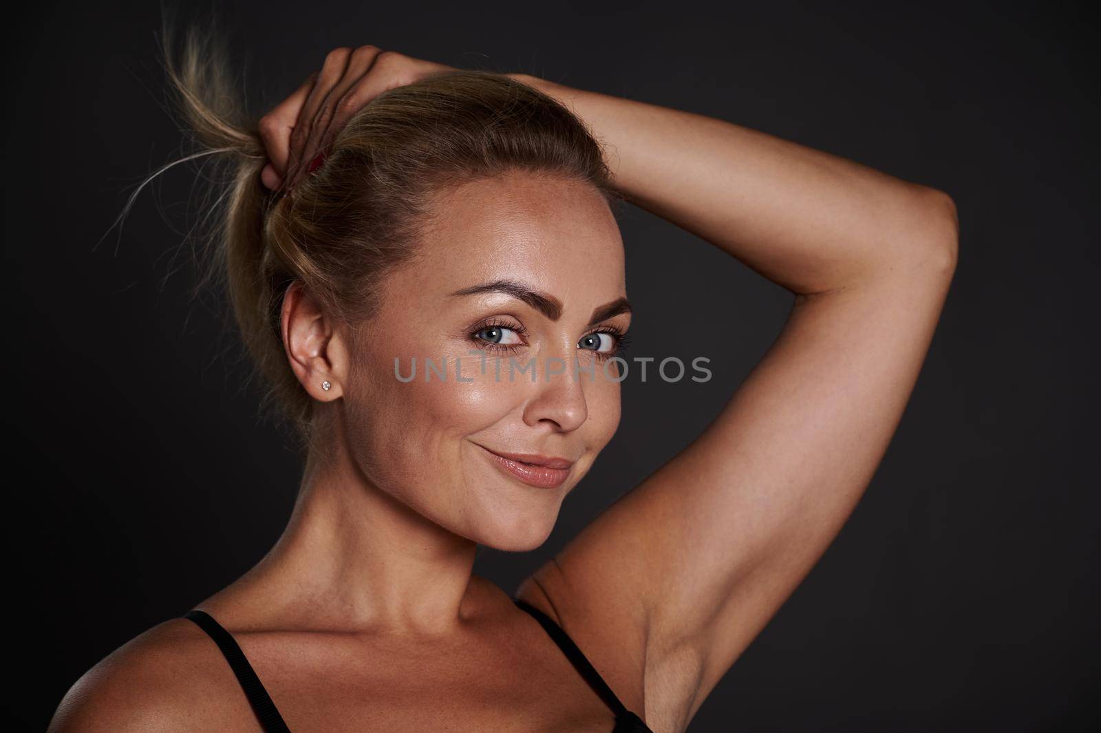 Attractive middle aged European woman cutely smiles looking at camera isolated over black background with copy ad space. Anti-aging, smoothing, rejuvenation beauty therapy