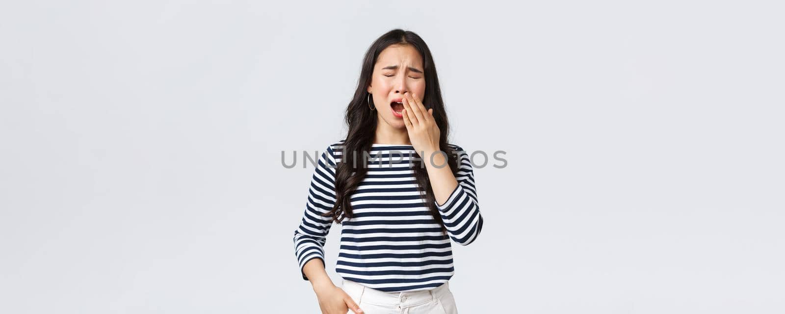 Lifestyle, people emotions and casual concept. Sleepy tired woman working late in office, close eyes and yawning, want go bad. Asian girl woke up early, need coffee, stand white background.