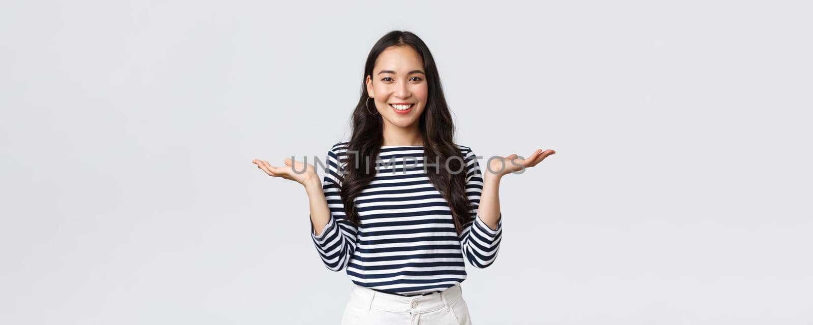Lifestyle, people emotions and casual concept. Cute smiling asian woman introduce two products, hold hands sideways as if demonstrating products on palms, standing white background.